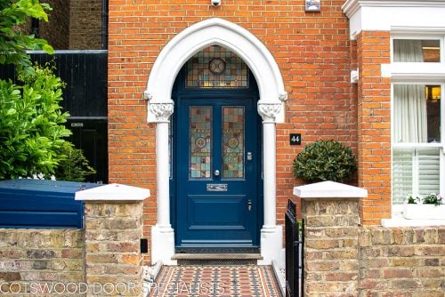 Extra wide Victorian front entrance door painted blue with stained glass. Door frame with glass to the sides and above the door