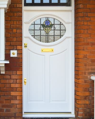 White 1920s front door with oval stained glass. Brass door furniture