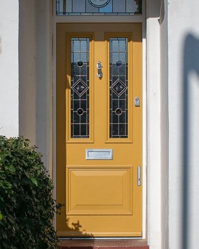 painted yellow Victorian front entrance door and frame with stained glass. Number in glass above door