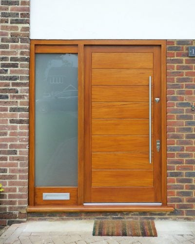 Wide boarded contemporary front door. Sidelight frame with etched glass. Simple door furniture with long bar handle. Satin chrome banham locks
