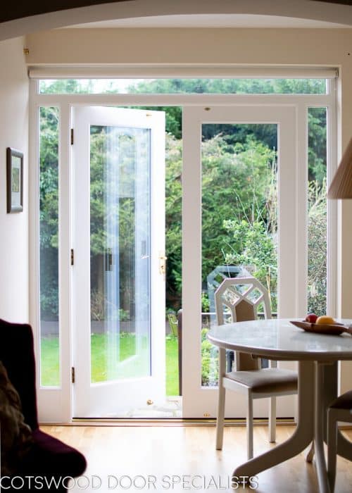 White painted wooden glazed french door with sidelight frame. Double glazed clear glass and brass hardware. Doors opening into garden