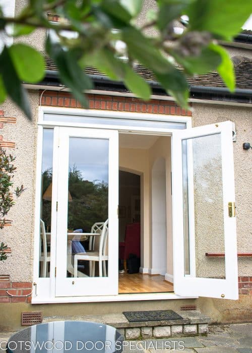 White painted wooden glazed french door with sidelight frame. Double glazed clear glass and brass hardware. Doors opening into garden