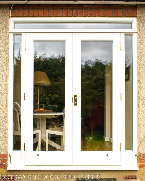 White painted wooden glazed french door with sidelight frame. Double glazed clear glass and brass hardware. Doors opening into garden