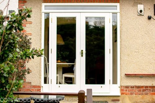 White painted wooden glazed french door with sidelight frame. Double glazed clear glass and brass hardware. Doors opening into garden