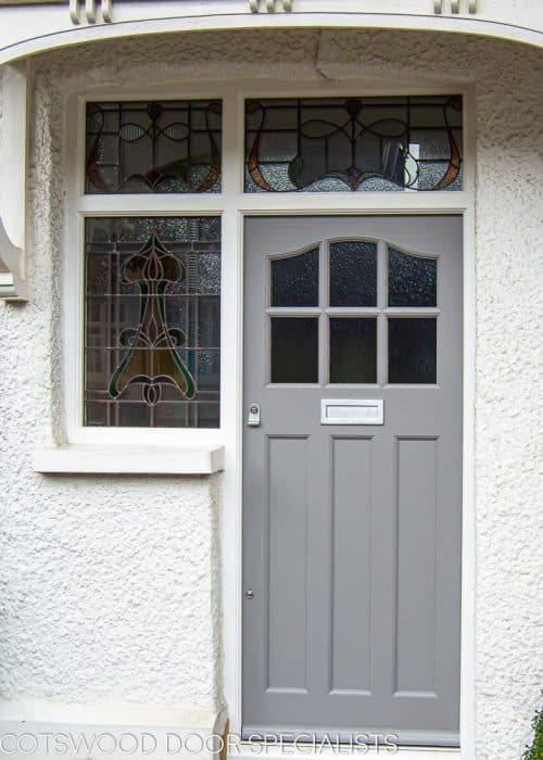 1930's External front door with sidelight door frame. Wooden door with six obscure glass panes. Door frame has three stained glass panes. Door painted grey and frame painted white. Satin chrome door furniture. Shot showing canopy. This door has an elegant curve at the head of the door, six glazing apertures and three flat panels.