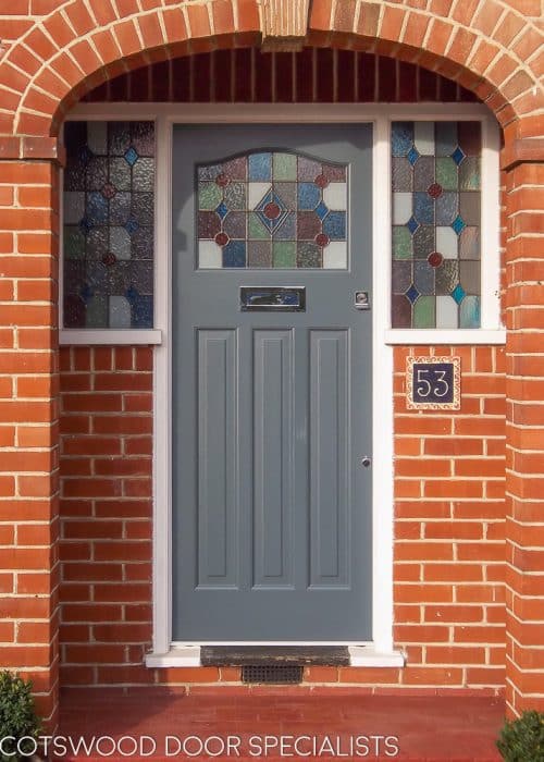 1930s style stained glass door. Front door painted light grey with a white door frame. London house with red brickwork. Wooden door. Leaded glass with different colours. Polished chrome door furniture.