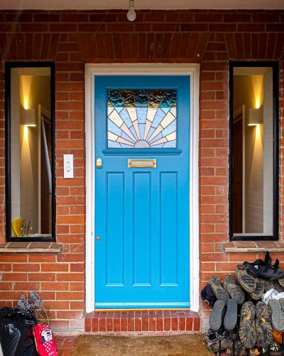 Art Deco front door painted bright blue. Art deco sunrise stained coloured glass. Antique brass door furniture. Fitted into an existing door frame in London