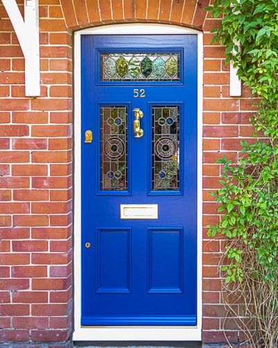 Dark blue Edwardian door with stained glass fitted into open porch. Door has beautiful leaded light glass in a geometric design. Polished brass letterplate, door knob and door furniture.