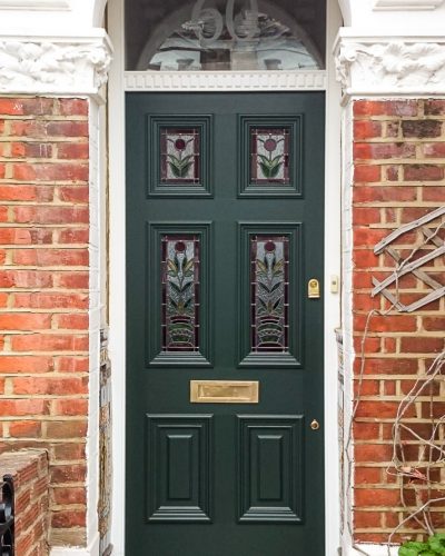 Stained glass Georgian front door fitted in London. Decorative door frame with dental block to transom. Original stained glass design with flowers. Door painted dark green with brass door furniture