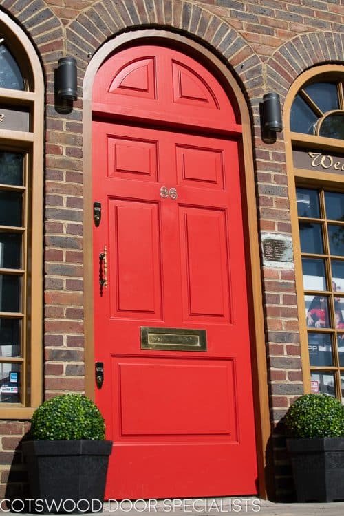 Red Georgian 5 panel front door fitted into an arched door frame. Solid door and frame with no glass painted bright red. Raised solid door panels. Polished brass door furniture.