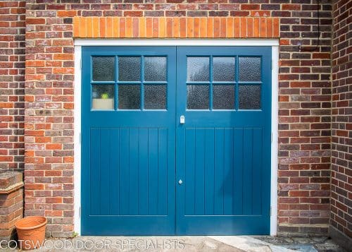 1930s wooden garage doors with matching front door. Fitted into a 1930s house with red brickwork. Doors painted dark blue. Front door has stained glass, garage doors have traditional textured obscure glass. Satin chrome door hardware