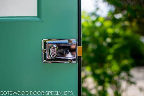 1930s art deco garage doors. Classic 1930's side hinged garage doors with glazing. Glazing is divided into 6 pieces per door with wooden glazing bar. Obscured glass. Painted light green. Tongue and groove style boarding. polished chrome door furniture. Close up of Yale lock.