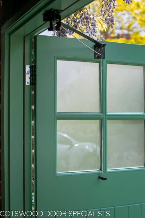 1930s art deco garage doors. Classic 1930's side hinged garage doors with glazing. Glazing is divided into 6 pieces per door with wooden glazing bar. Obscured glass. Painted light green. Tongue and groove style boarding. polished chrome door furniture. Close up of left door stay.
