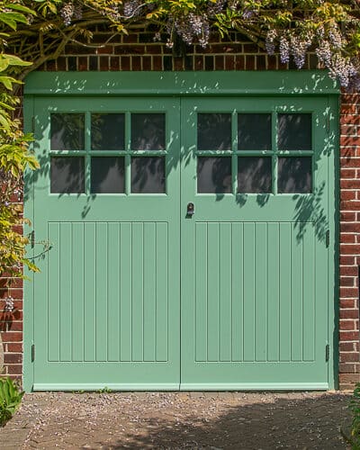 1930s art deco garage doors. Classic 1930's side hinged garage doors with glazing. Glazing is divided into 6 pieces per door with wooden glazing bar. Obscured glass. Painted light green. Tongue and groove style boarding. Polished chrome door furniture.
