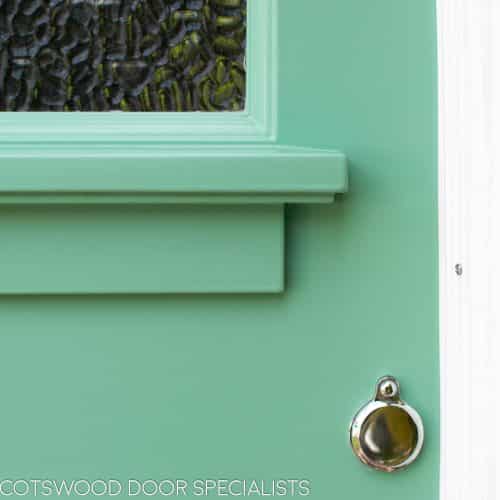 Art Deco glazed 1930s front door. Wooden glazing bar dividing glass into multiple panes. Textured Arctic obscured glass. Detailed shelf and moulding details to bottom half of door. 1930's green colour. Wisteria around door. Closeup of shelf detail