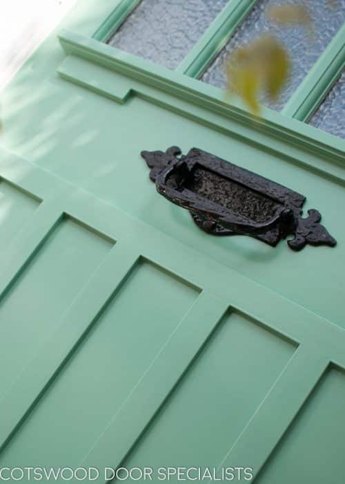 Art Deco glazed 1930s front door. Wooden glazing bar dividing glass into multiple panes. Textured Arctic obscured glass. Detailed shelf and moulding details to bottom half of door. 1930's green colour. Wisteria around door. Closeup of panel and letterplate