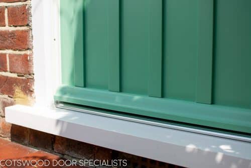 Art Deco glazed 1930s front door. Wooden glazing bar dividing glass into multiple panes. Textured Arctic obscured glass. Detailed shelf and moulding details to bottom half of door. 1930's green colour. Wisteria around door. Closeup of panel