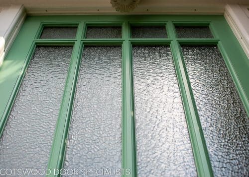 Art Deco glazed 1930s front door. Wooden glazing bar dividing glass into multiple panes. Textured Arctic obscured glass. Detailed shelf and moulding details to bottom half of door. 1930's green colour. Wisteria around door. Closeup of wooden glazing bar