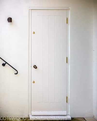 Cottage style back door. White painted wooden back door and frame. Cottage style boarded door. Antique brass door furniture