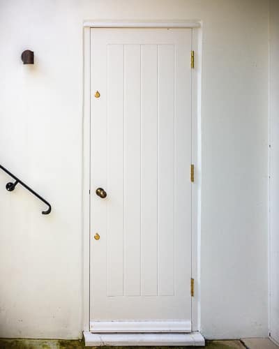 Cottage style back door. White painted wooden back door and frame. Cottage style boarded door. Antique brass door furniture