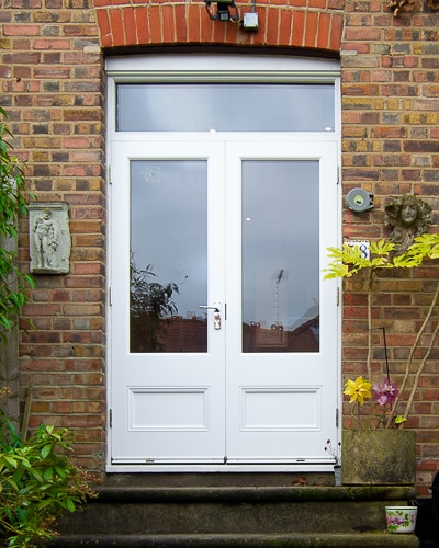 Wooden French doors fitted into a London home. Doors leading out to the garden from kitchen. Flat panels to bottom of doors with traditional panel mouldings. Doors and frame double glazed and painted white