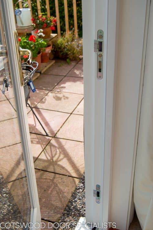 Wooden bifolding doors. White painted wooden bifolds at back of large house. Fully glazed with clear double glazed units. Sliding on track to enable doors to fully open. Closeup of security locking system