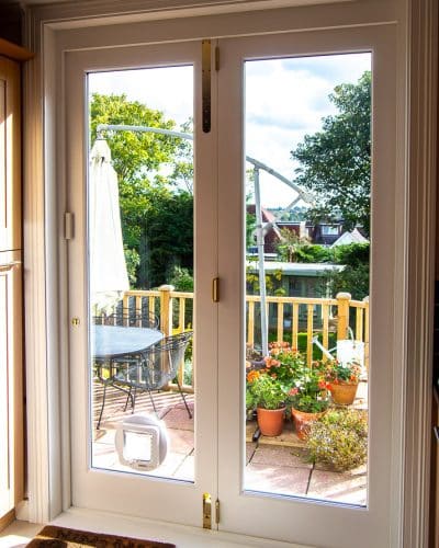 Wooden bifolding doors. White painted wooden bifolds at back of large house. Fully glazed with clear double glazed units. Sliding on track to enable doors to fully open