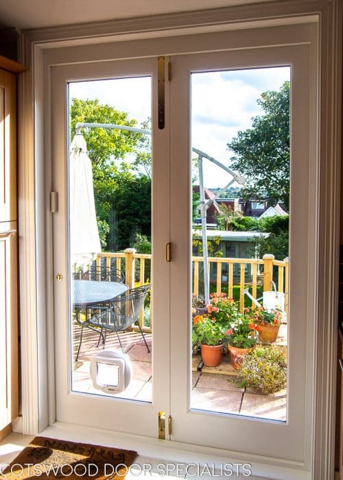 Wooden bifolding doors. White painted wooden bifolds at back of large house. Fully glazed with clear double glazed units. Sliding on track to enable doors to fully open