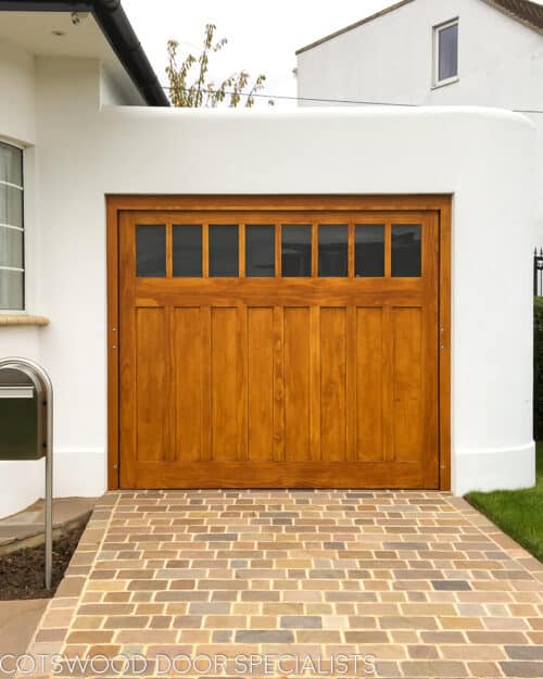 bespoke accoya deco garage door. Art deco electrically operated garage door fitted into a 1930s residence. Picture from front of house showing classic crittall bay windows. Stained natural accoya wooden door with frame. Etched glass to top of door.. simple flat panels with minimal mouldings