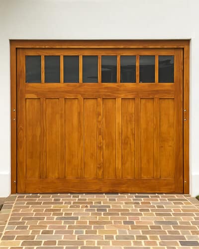 bespoke accoya deco garage door. Art deco electrically operated garage door fitted into a 1930s residence. Picture from front of house showing classic crittall bay windows. Stained natural accoya wooden door with frame. Etched glass to top of door. simple flat panels with minimal mouldings