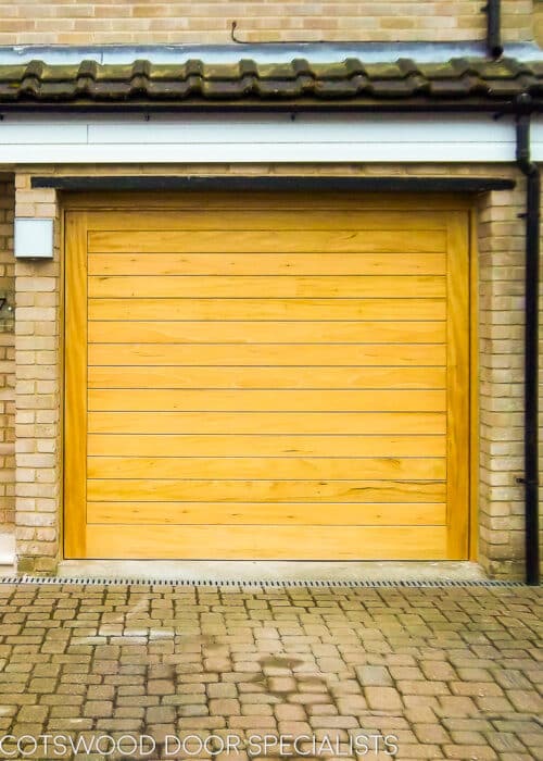 contemporary wooden up and over garage door. Electrically operated garage door made of wood. Light coloured stained wood with matching front door.