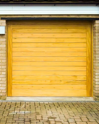 contemporary wooden up and over garage door. Electrically operated garage door made of wood. Light coloured stained wood with matching front door.