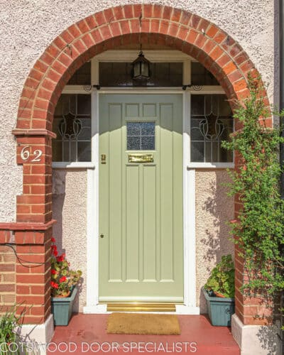 1920s Front door fitted into an arch, making an open storm porch. door is painted light green with a red brick arch surrounding. Door and door frame have stained leaded glass. Door has recessed flat panels for a non fussy appearance.