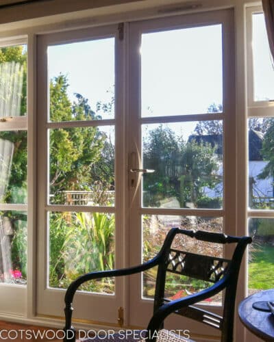 1930s French door with opening windows. Wooden French door fully painted white with clear double glazed glass. Doors and side windows leading out onto garden. Brass door handles