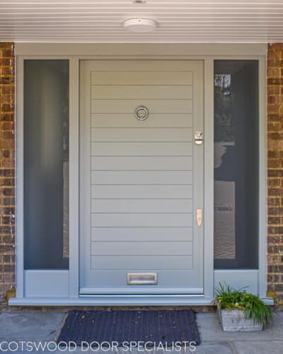 Contemporary external door. Wide wooden door with horizontal boards painted in a green grey colour. Etched glass to sidelights. Satin chrome door furniture