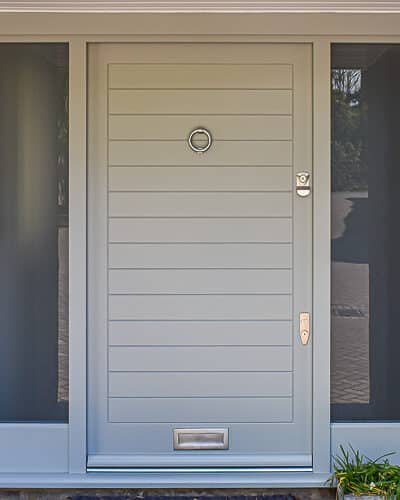 Contemporary external door. Wide wooden door with horizontal boards painted in a green grey colour. Etched glass to sidelights. Satin chrome door furniture