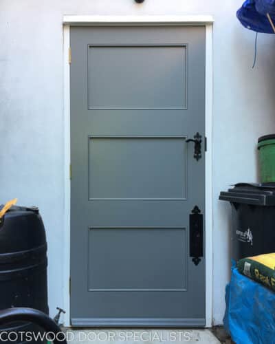 Contemporary side door to house. Door is painted grey surrounded by white rendered walls. Bespoke black iron door furniture.