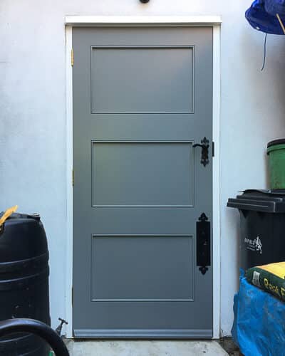 Contemporary side door to house. Door is painted grey surrounded by white rendered walls. Bespoke black iron door furniture.