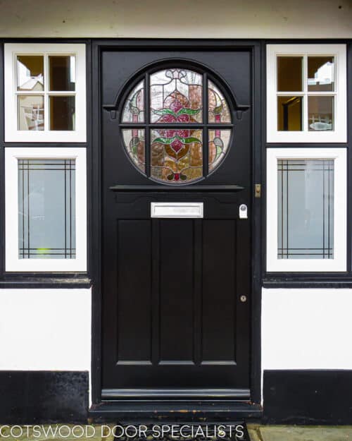 Edwardian stained glass door. Glass is oval shaped and divided with wooden glazing bar. The door is fitted into a frame with surrounding windows. Door painted black and the door frame is white and black