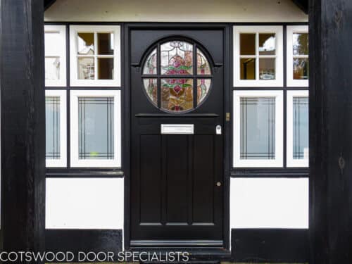 Edwardian stained glass door. Glass is oval shaped and divided with wooden glazing bar. The door is fitted into a frame with surrounding windows. Door painted black and the door frame is white and black