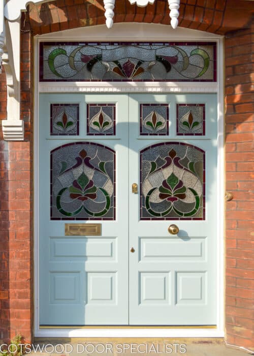 Edwardian stained glass doors. Pair of Edwardian front doors with an ornate stained glass design. Doors fitted into open porch with decorative roof. Red brick surrounding painted light blue doors. Antique brass door furniture. Period stained glass replicating original Edwardian design
