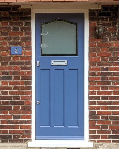 Etched glass 1930s door. Wooden door is painted blue fitted into a red brick london home. Door has etched glass with a simple clear border. Door furniture is stain chrome. New door frame is painted white