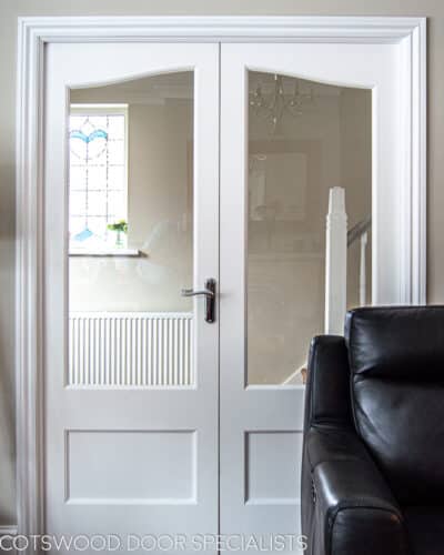Glazed double doors. White painted bespoke doors with clear glass. Leading into hallway from sitting room. Doors have panel in bottom section and are fitted with polished chrome handles