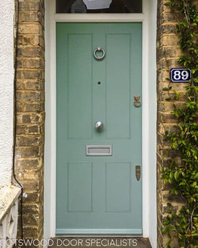 Green Victorian door fitted into a London home with yellow brickwork. Door has simple butt and beaded door panels. Satin chrome door furniture and security banham locks