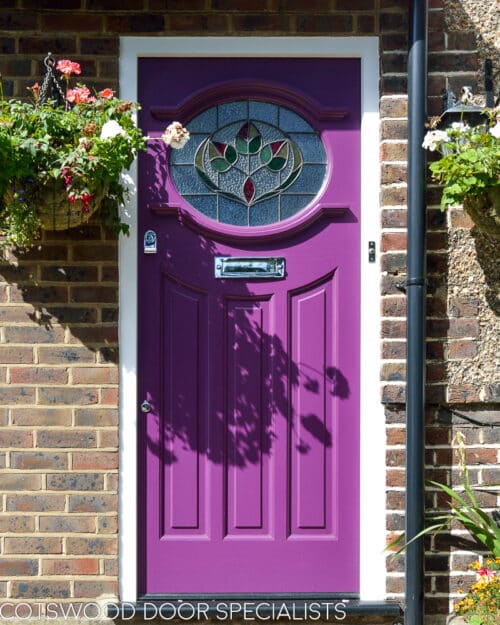 Purple 1930s front door with stained glass with leave design. Oval shaped stained glass pane. Polished chrome door furniture. door fitted into a london red brick home. Garage door painted same colour as front door