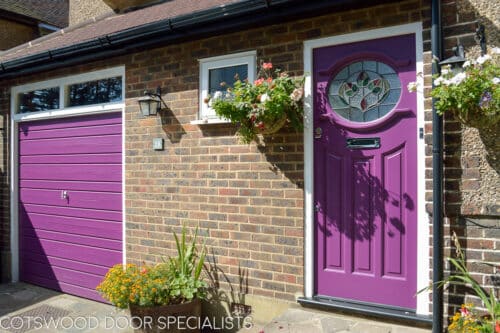 Purple 1930s front door with stained glass with leave design. Oval shaped stained glass pane. Polished chrome door furniture. door fitted into a london red brick home. Garage door painted same colour as front door