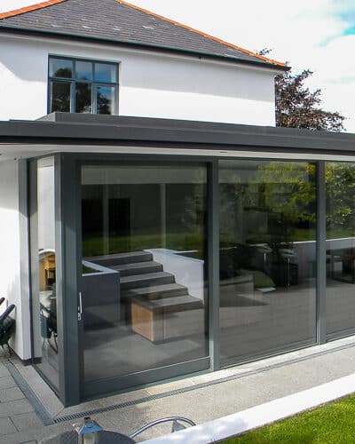 Sliding wooden door. Grey painted wooden doors with clear double glazed units. Fitted into a contemporary home with white rendered walls. Doors leading out onto patio area from the kitchen .Doors are section of large glazed bay