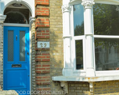 Tall Blue Victorian door. An extra tall Victorian door painted light blue. Fitted into a North London terraced home. Etched glass with a repeated pattern. Polished chrome door furniture. Photo showing door and bay window