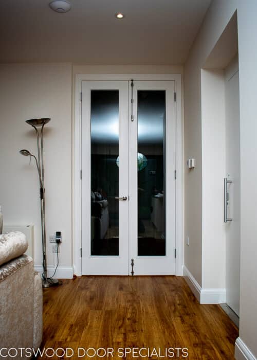 Tall white painted wooden internal fire doors with clear glass. Fitted onto hallway with satin chrome door furniture.