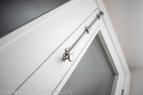 Tall white painted wooden internal fire doors with clear glass. Fitted onto hallway with satin chrome door furniture. Closeup shot of long shoot bolt